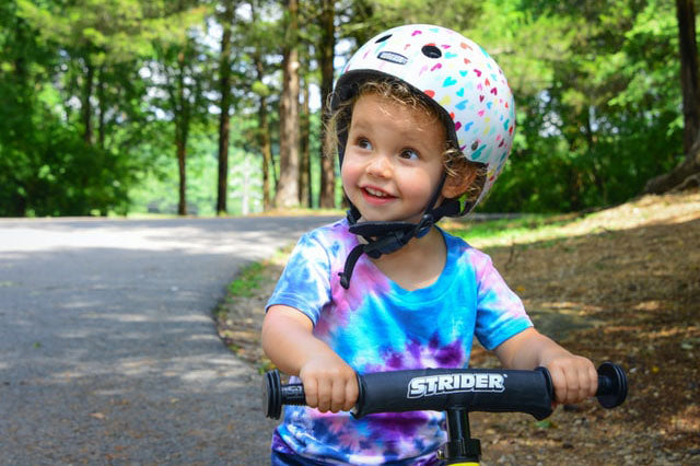 Little girl riding scooter with helmet and wearing tie dye shirt