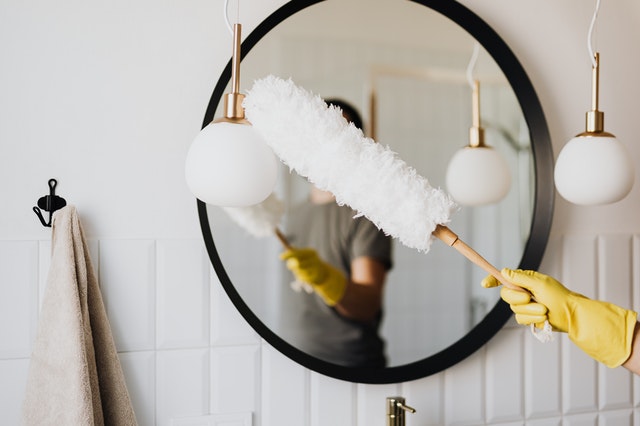 Woman dusting bathroom mirror.