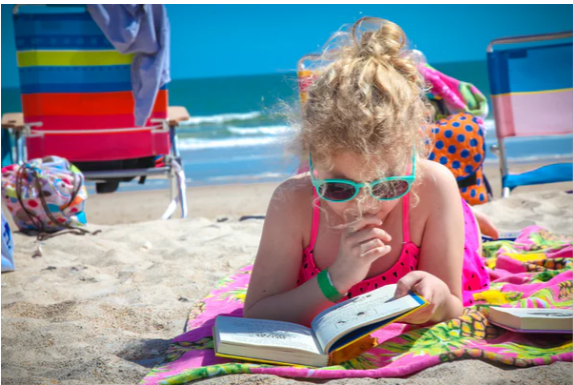 Little girl laying on beach reading