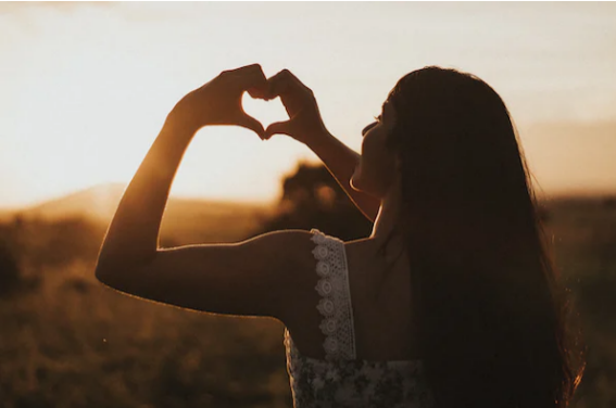woman standing in sunlight with heart hands