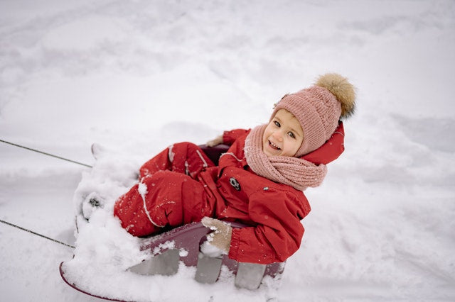 Child in a red snowsuit being pulled on a sled.
