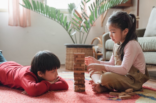 Children playing with a wooden block tower on the floor
