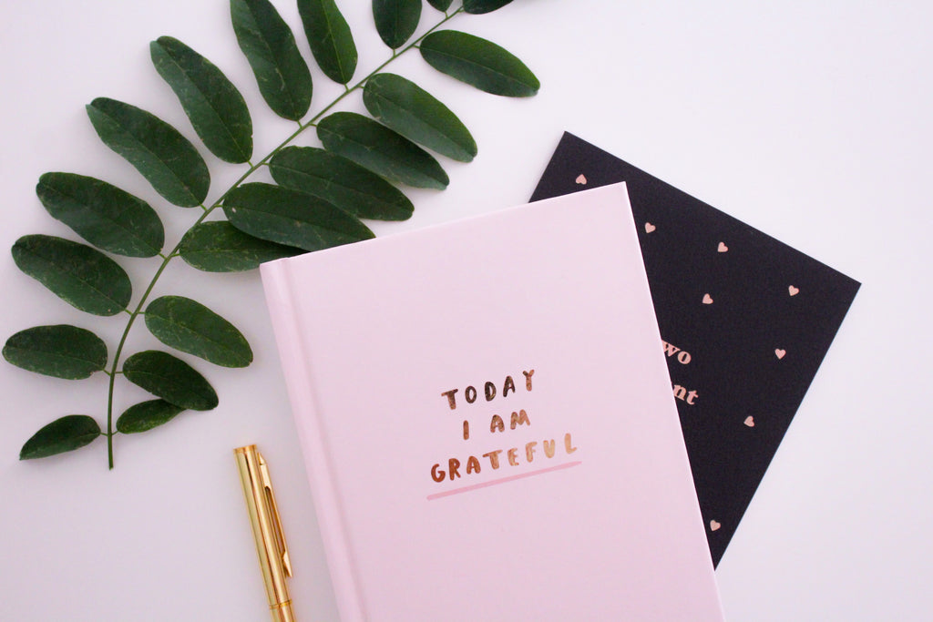 Pink "Today I Am Grateful" journal next to gold pen.