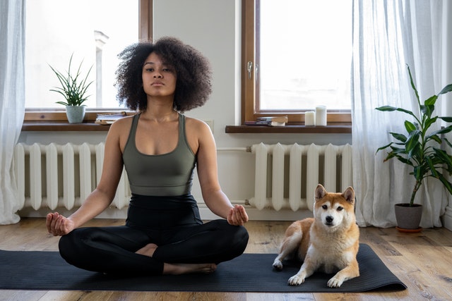 Woman sitting cross-legged on yoga mat with dog next to her.