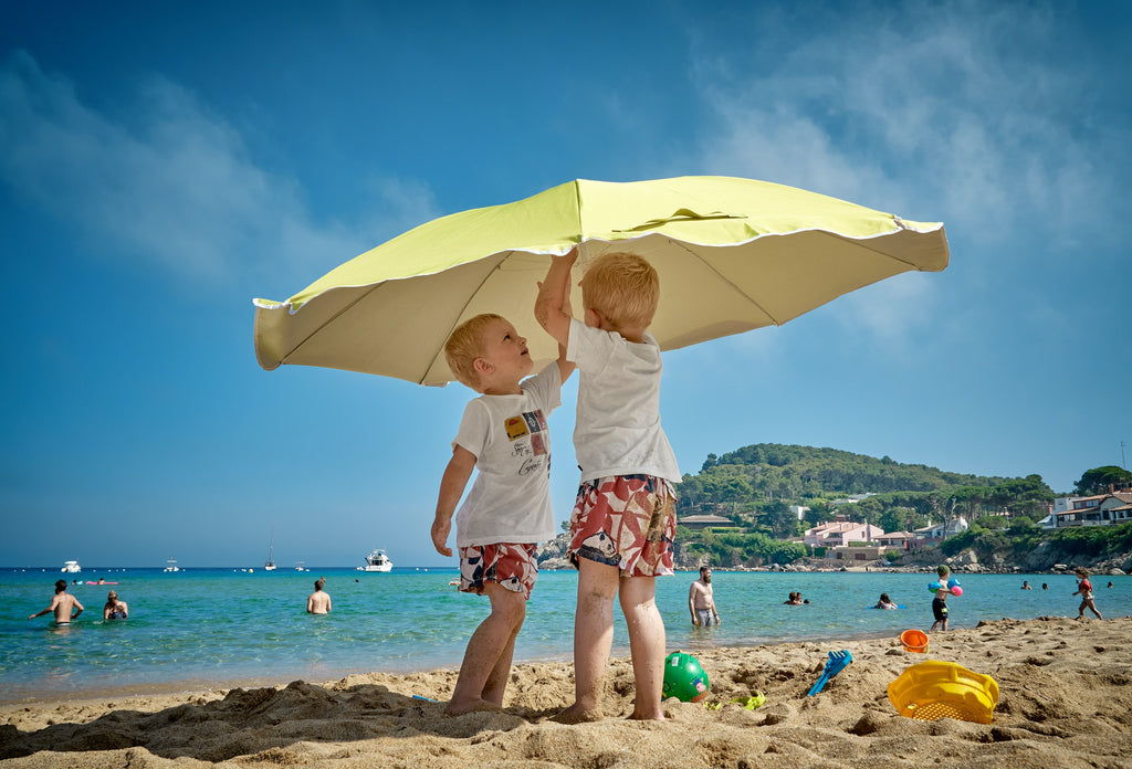 Children holding umbrella on beach.